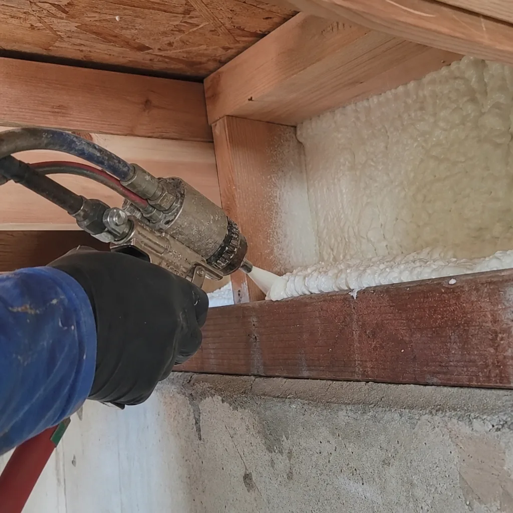 Worker applying expanding spray foam insulation to a residential building foundation